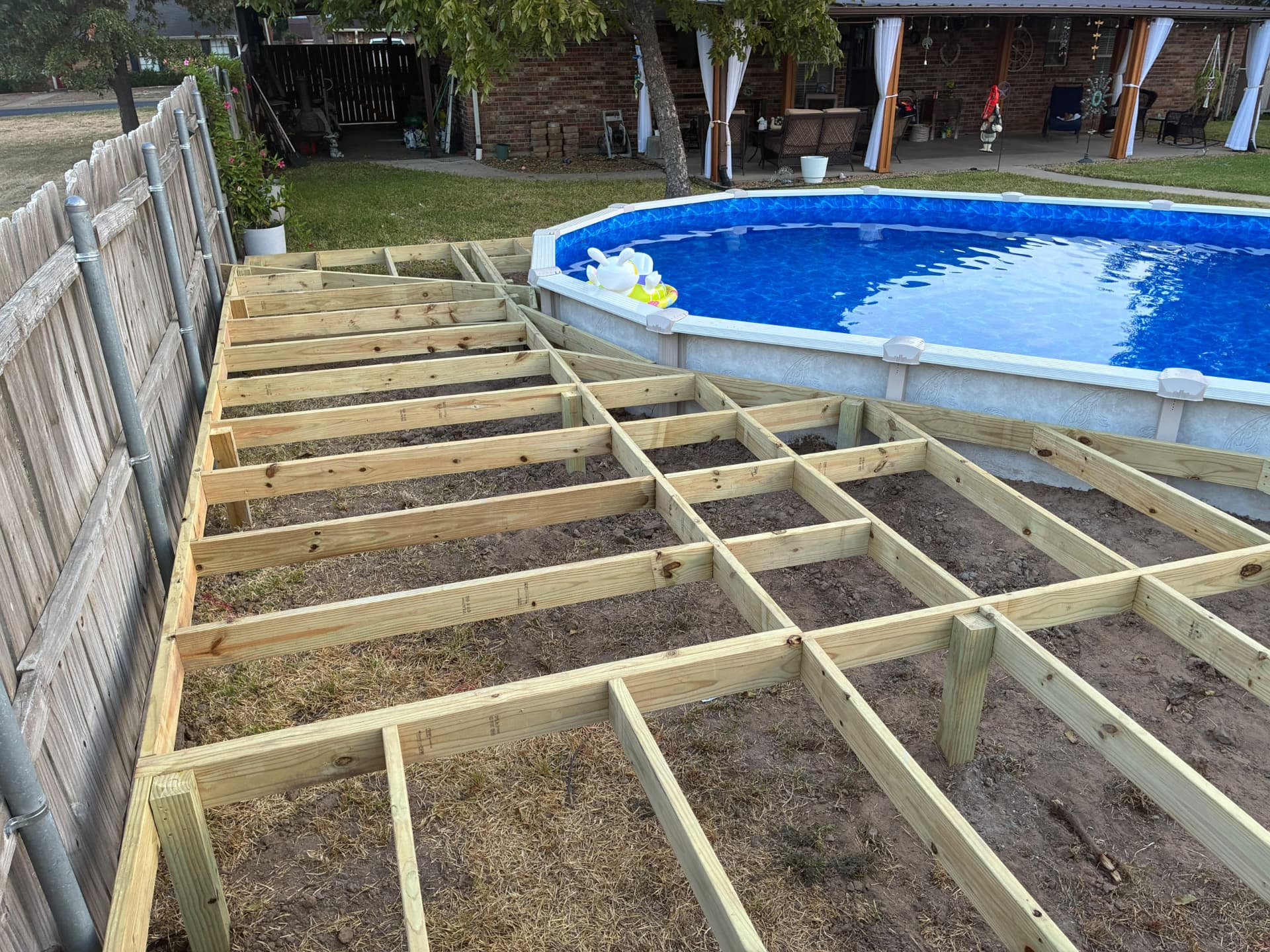 Angled pressure treated joists fitted along the pool wall beside the fence, built by BenchMark Decks in Mabank, Texas