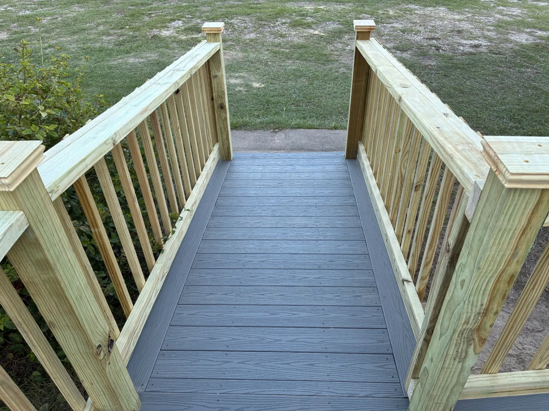 Bottom of a composite ramp with handrails and post caps, built by BenchMark Decks in Trinity, Texas