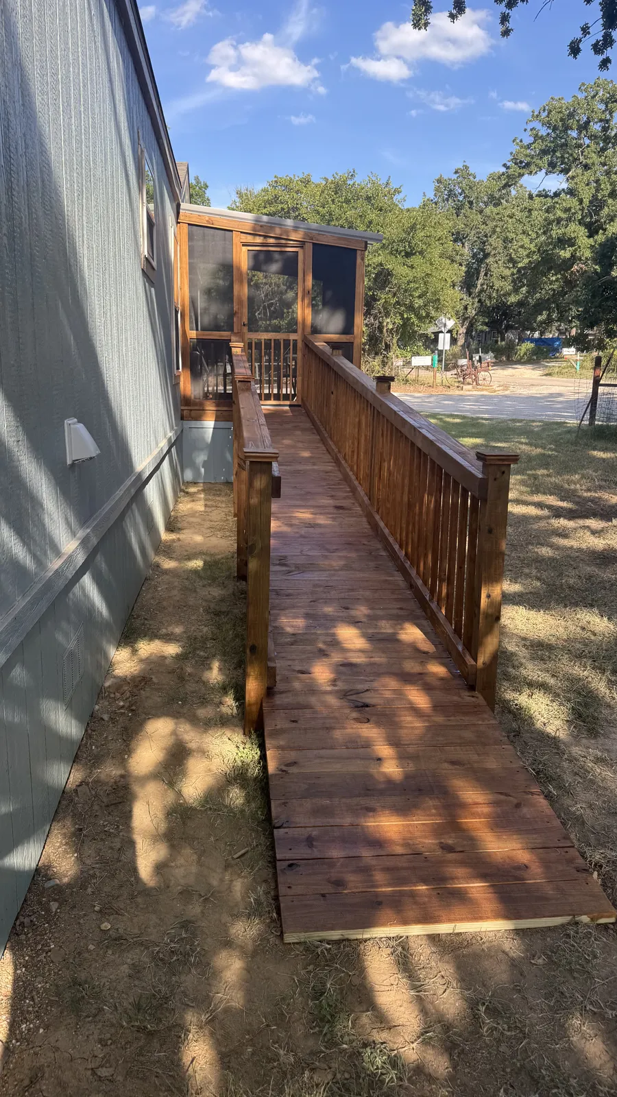 Long wood ramp with handrails leading to a screened porch on a mobile home, built by BenchMark Decks in Cleburne, Texas