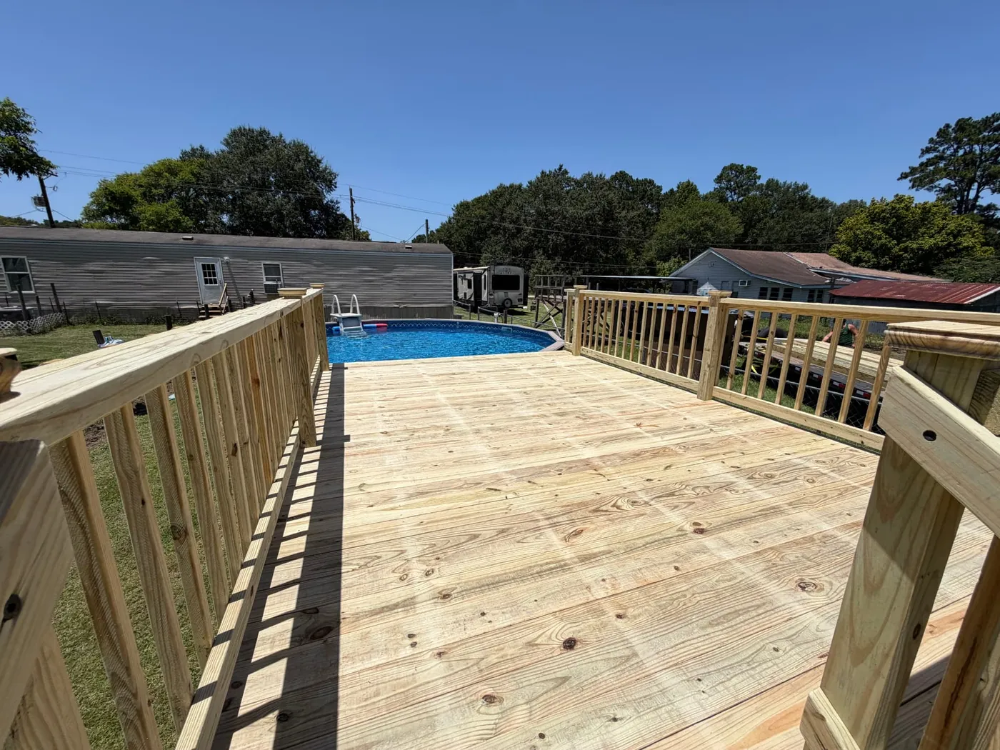 Large pressure-treated pool deck with railing beside an above-ground pool