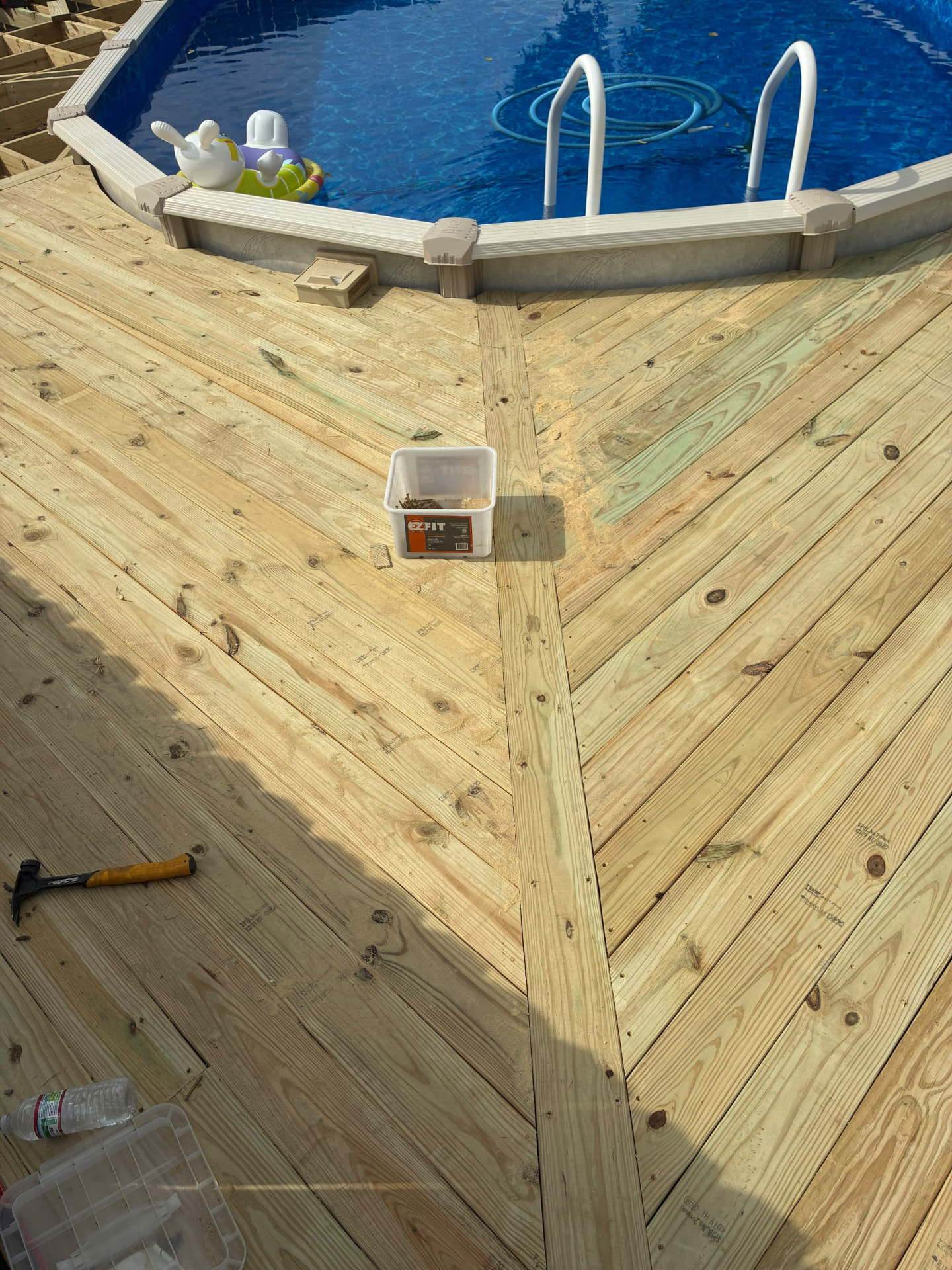Pressure treated deck boards laid in an angled pattern meeting at a center board by the pool ladder, built by BenchMark Decks in Mabank, Texas
