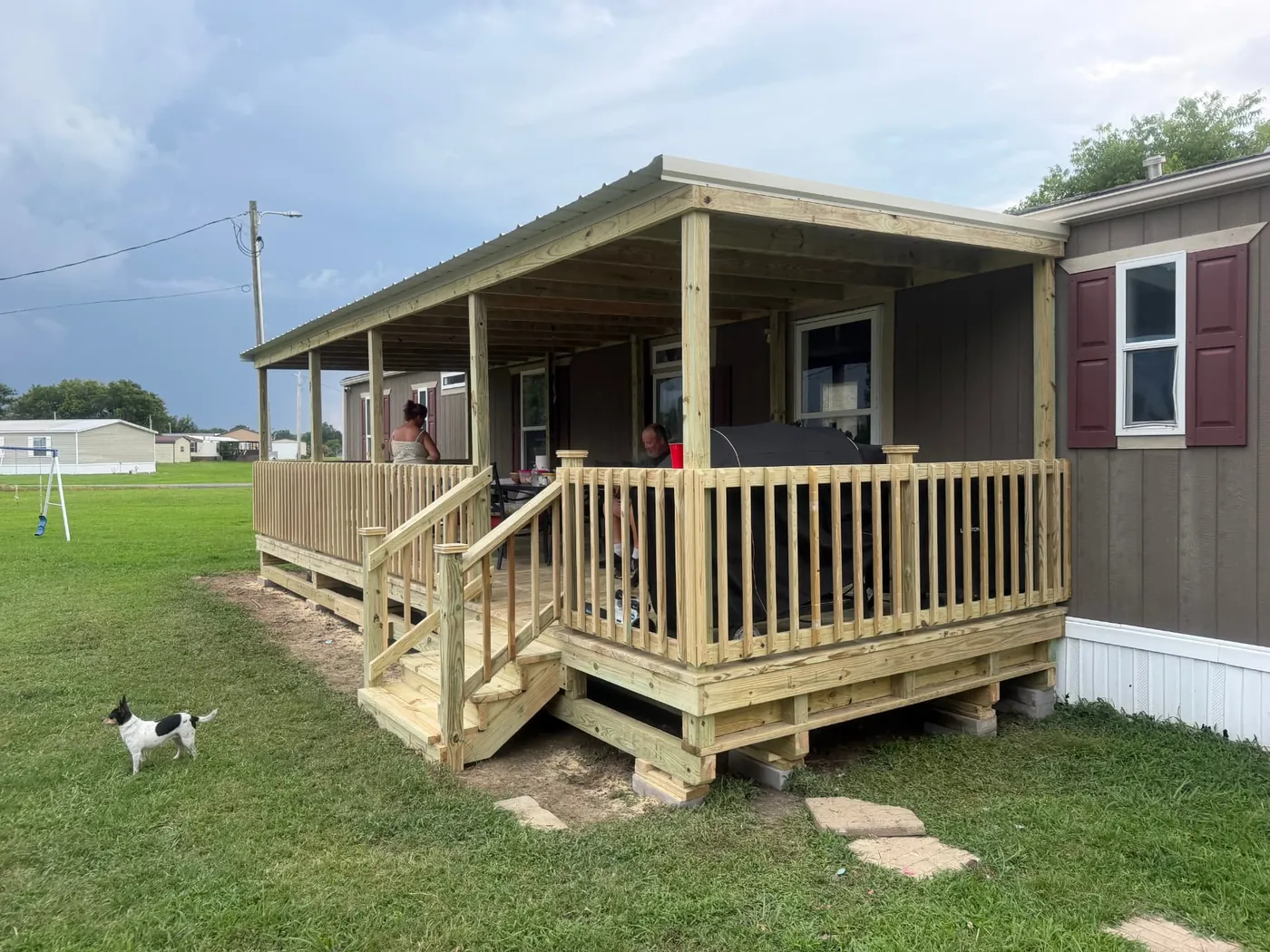Large covered mobile home deck with railing, stairs, and metal roof