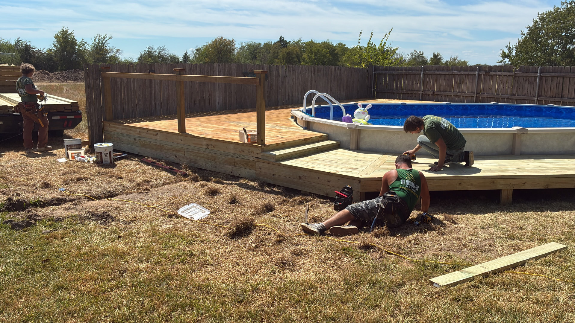 BenchMark crew installing skirting around Terri's pool deck while railing posts stand along the upper level, built by BenchMark Decks in Mabank, Texas