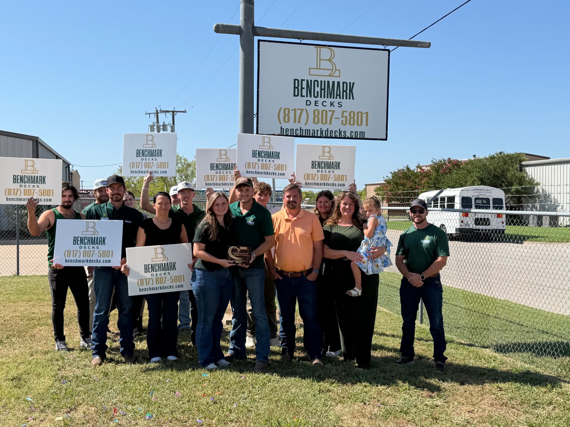 The BenchMark Decks team holding company yard signs at the Cleburne lot