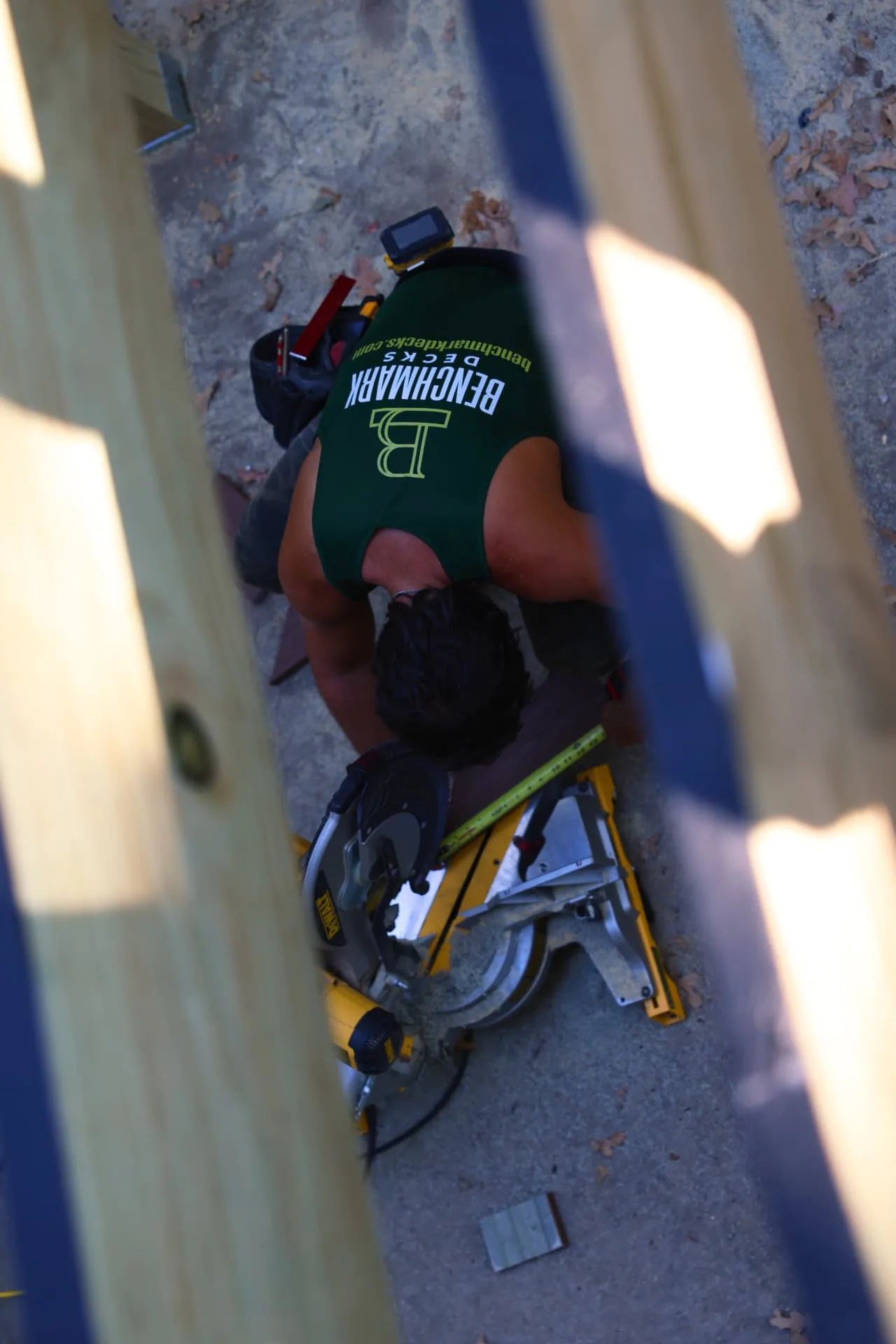 Benchmark Decks crew member cutting composite decking on a miter saw below the deck frame