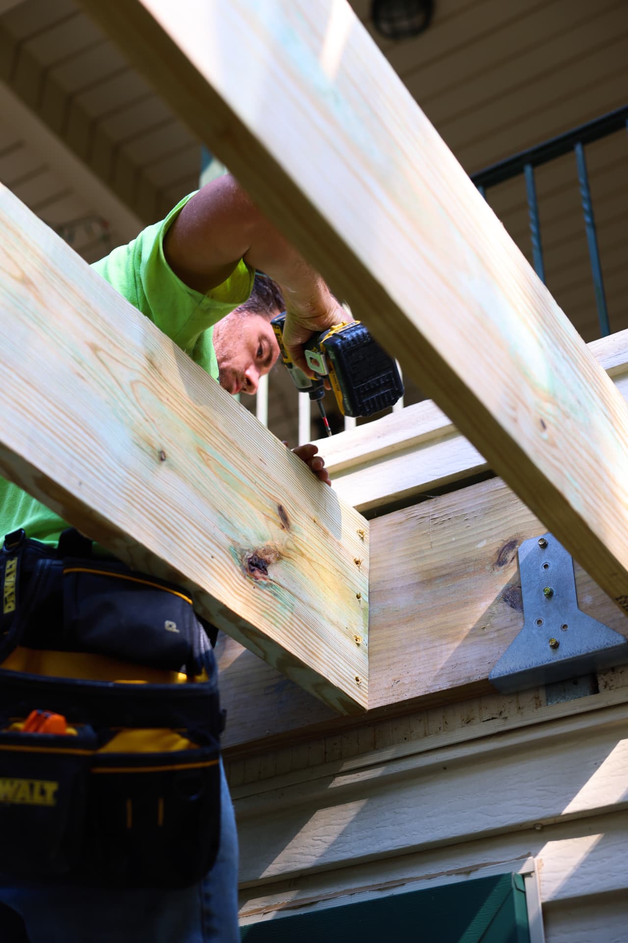 Installer driving structural fasteners into deck framing with galvanized hardware
