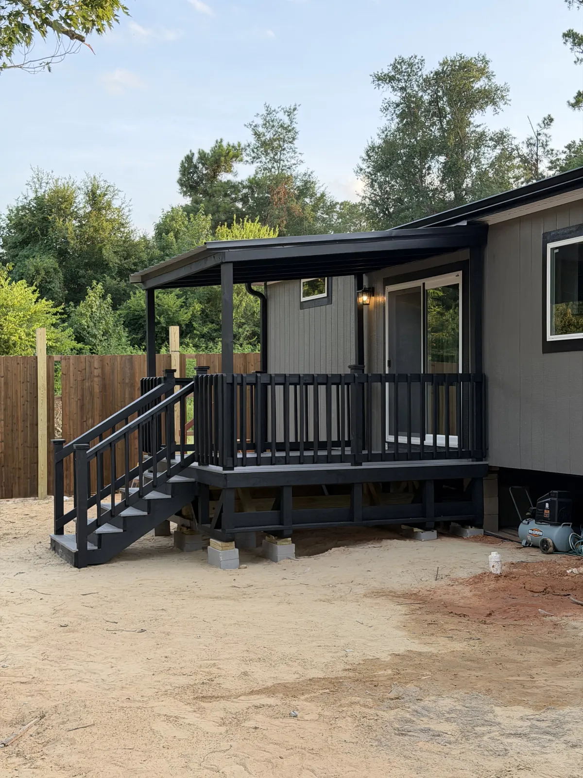 Black and gray covered back deck with metal roof, spindle railing and stairs on a new home, built by BenchMark Decks in Tyler, Texas