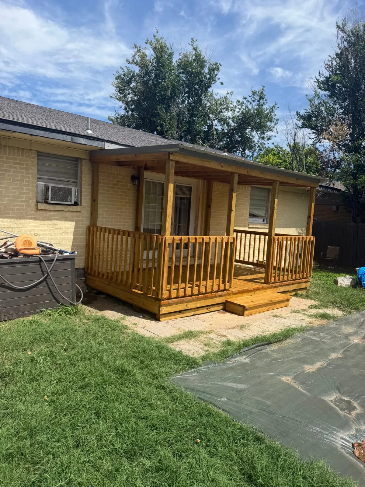 Covered treated wood deck with railing, metal roof and center steps on a brick home, built by BenchMark Decks in Lawton, Oklahoma