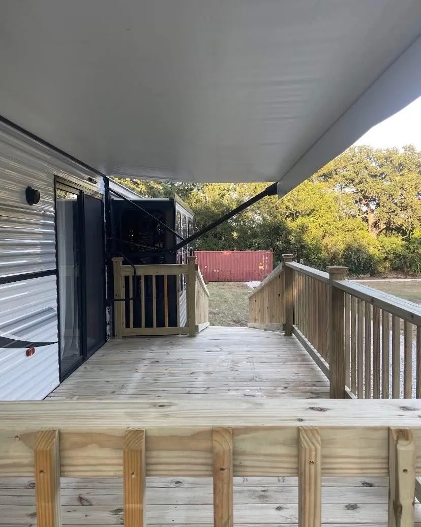 Covered RV deck with pressure-treated railing and stairs running alongside a travel trailer