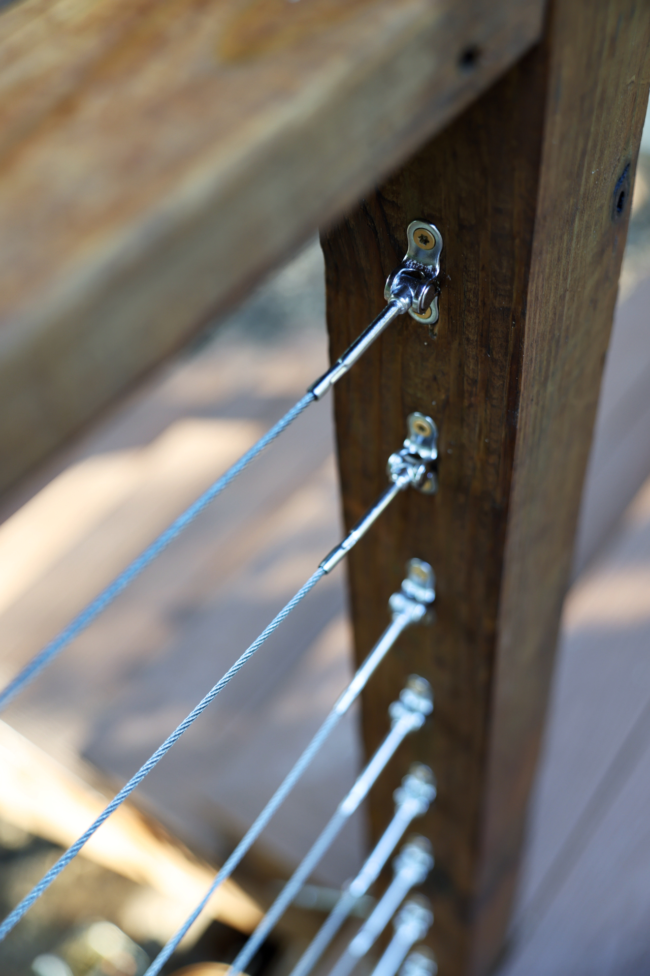 Close-up of stainless cable railing tensioners fastened to a stained deck post