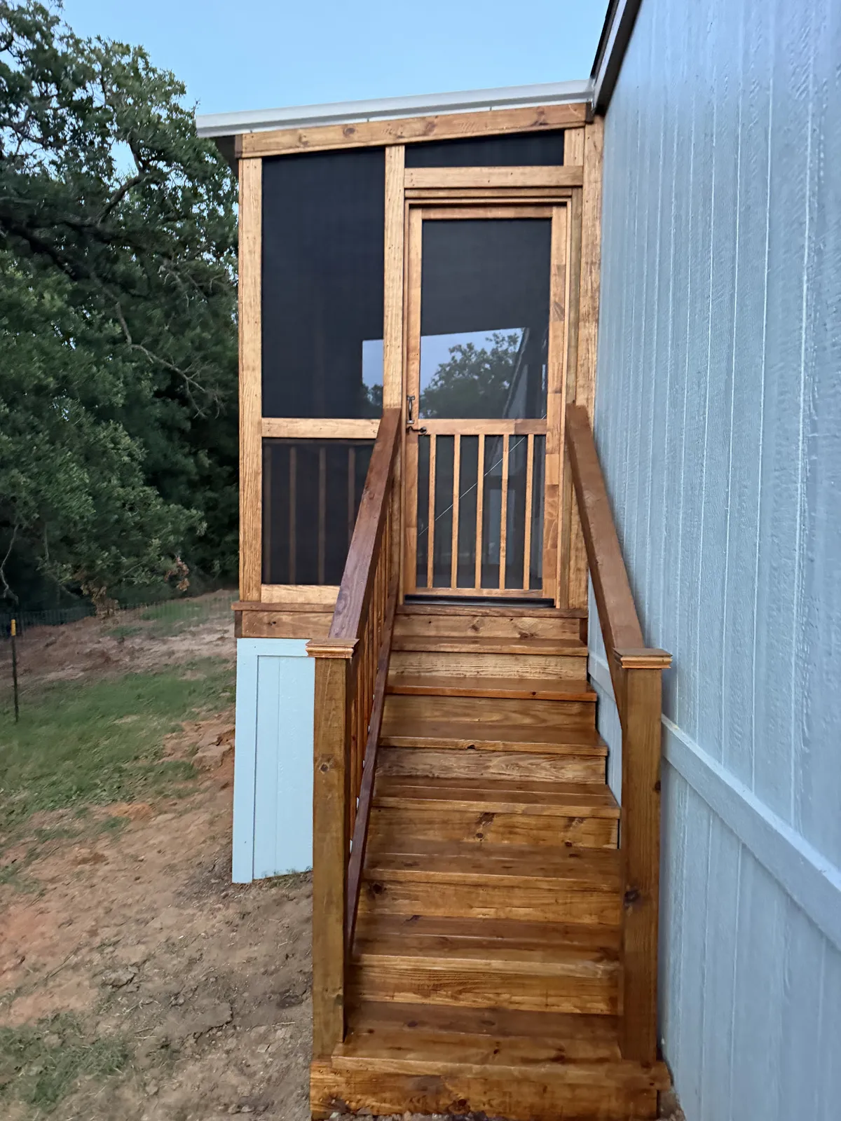 Stained wood entry steps with handrails up to a screened porch door on a mobile home, built by BenchMark Decks in Cleburne, Texas