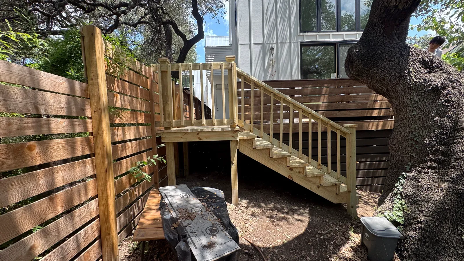 4x4 pressure treated deck with stairs and wood railing tied into an existing deck under live oaks, built by BenchMark Decks in Austin, Texas