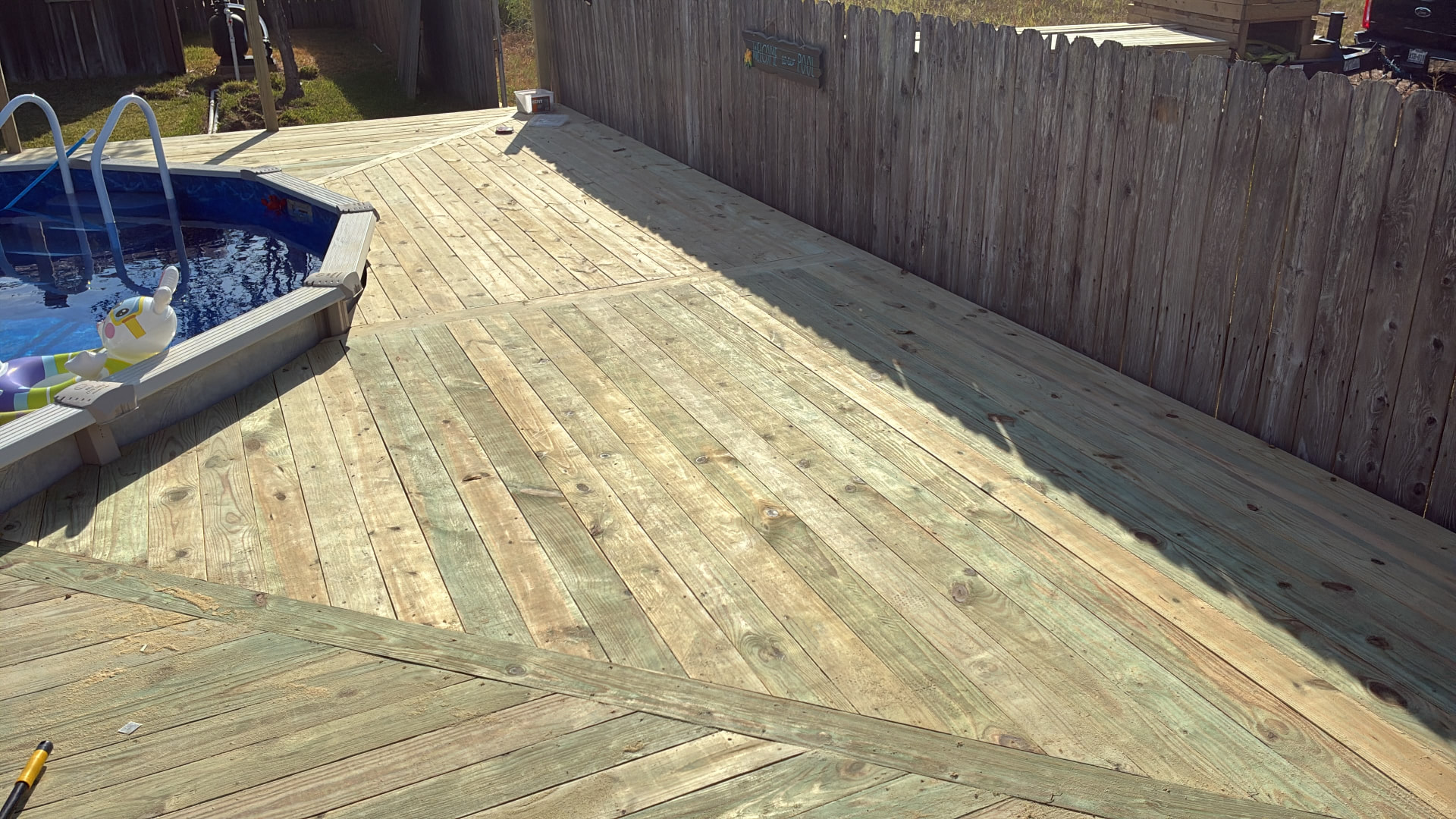 Pressure treated decking with picture-frame borders dividing angled board sections along the fence beside Terri's pool, built by BenchMark Decks in Mabank, Texas