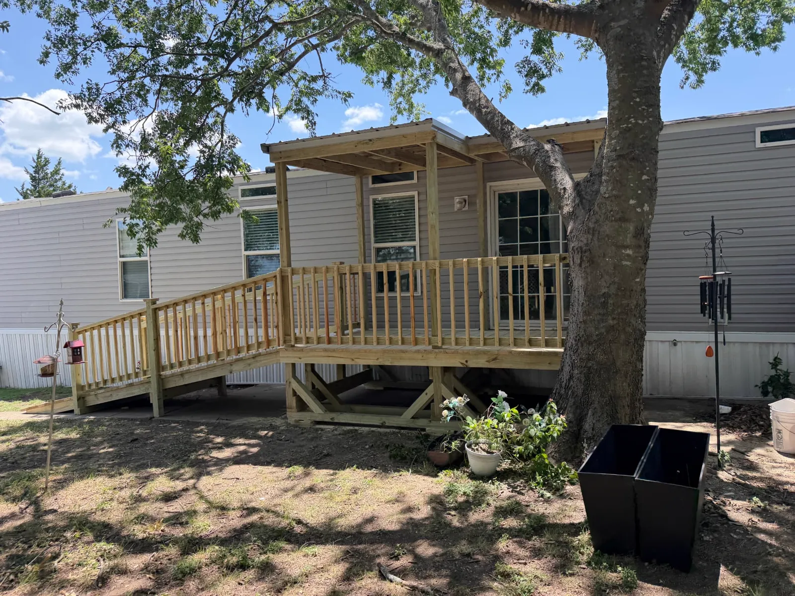Portable covered deck with ramp and wood railing beside a large shade tree, built by BenchMark Decks in Waxahachie, Texas