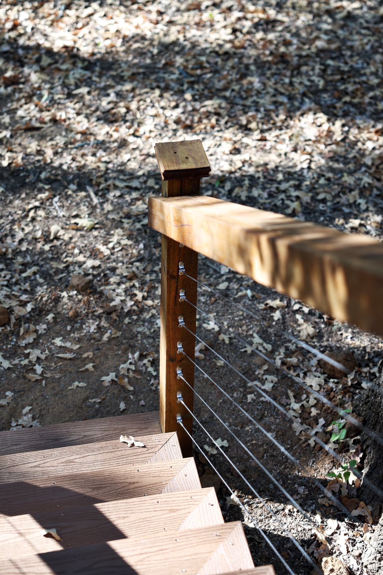 Cable railing tensioners on a stained stair post next to composite treads